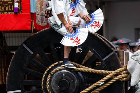 Men with fans above a hoko float wheel during the Yamaboko Junkō parade of the Gion Matsuri.